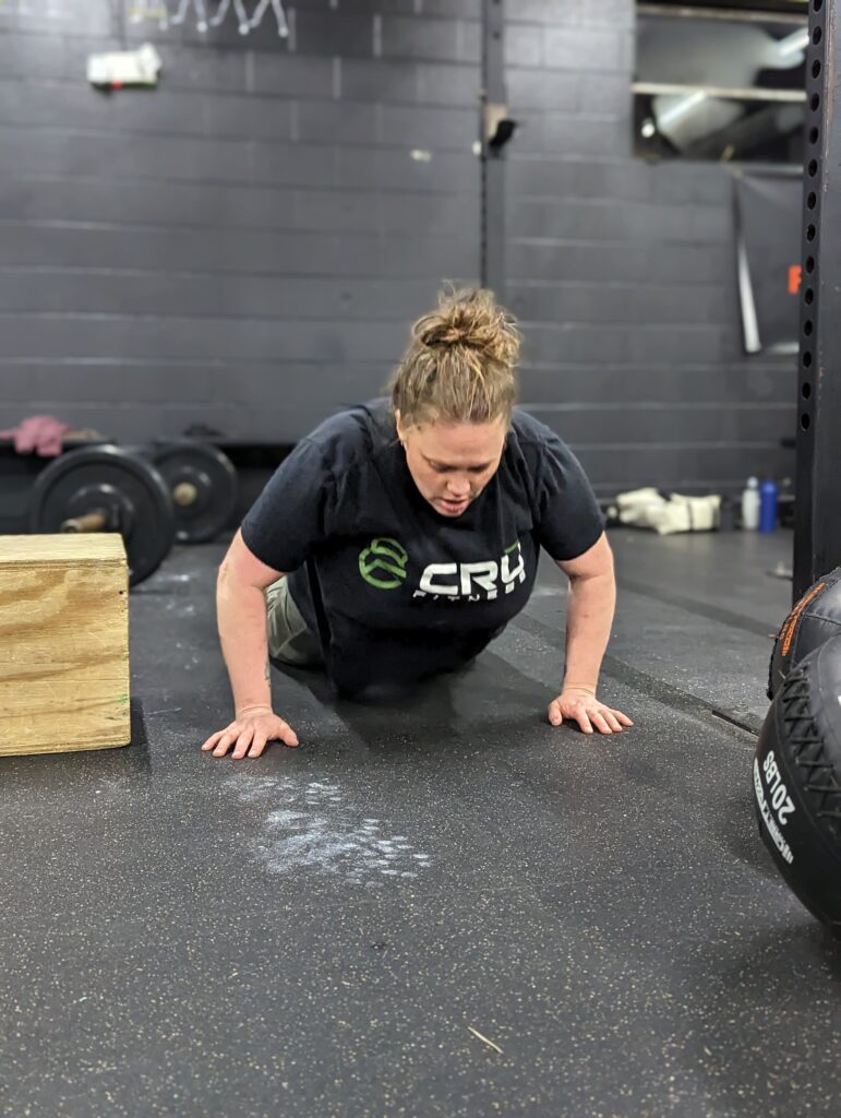 middle aged female gym member performing a burpee movement during a workout wearing a Crū fitness gym tshirt